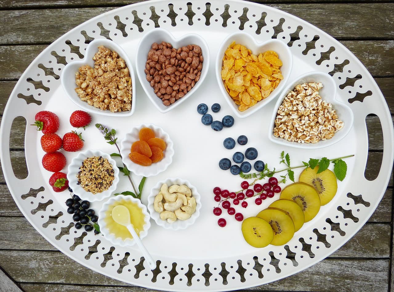 A white tray with fruits, nuts, cereals, and honey, arranged for a healthy, skin-nourishing diet.