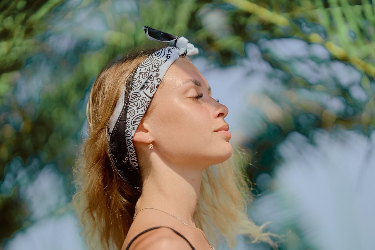 A relaxed woman with a bandana enjoys the sun, highlighting the importance of sun protection and a healthy outdoor lifestyle for glowing skin.