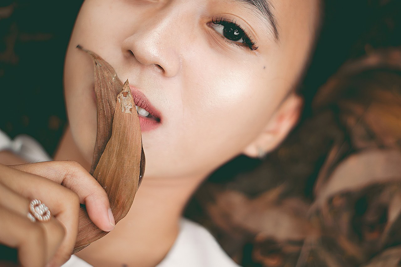 A close-up of a woman with radiant skin holding a dried leaf, symbolizing natural beauty, skincare, and the connection between nature and wellness.